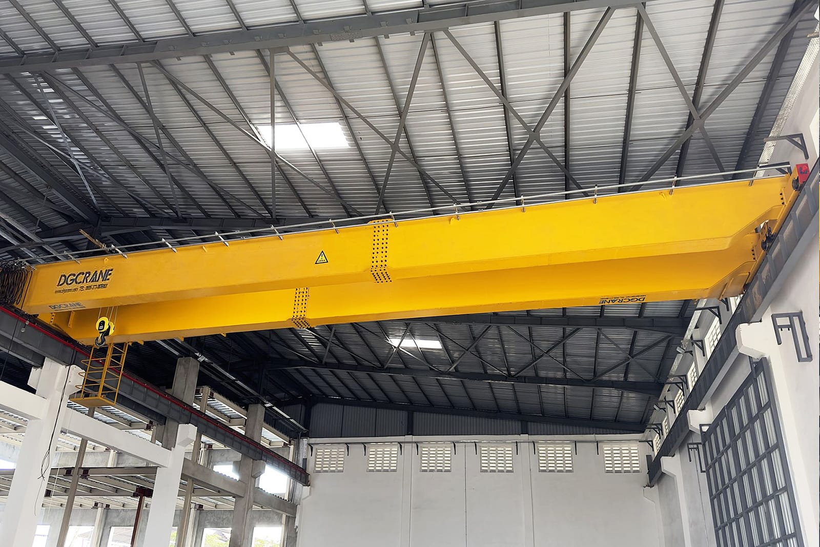 Een levendig gele dubbelligger-bovenloopkraan van het NLH-type met het merk DGCRANE, gemonteerd in een goed verlichte industriële omgeving met een dak van metalen platen en hoge ramen