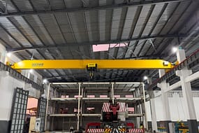  Żółta suwnica pomostowa FEM w standardzie FEM z brandingiem DGCRANE, zlokalizowana na dużym obszarze budownictwa przemysłowego z konstrukcjami metalowymi i ciężkimi maszynami poniżej