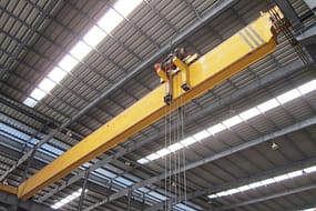  An offset single girder overhead crane with a yellow beam and a hoist, set in a large industrial warehouse.