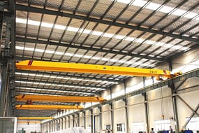  A series of single girder electric overhead travelling cranes with bright yellow beams inside a large industrial warehouse