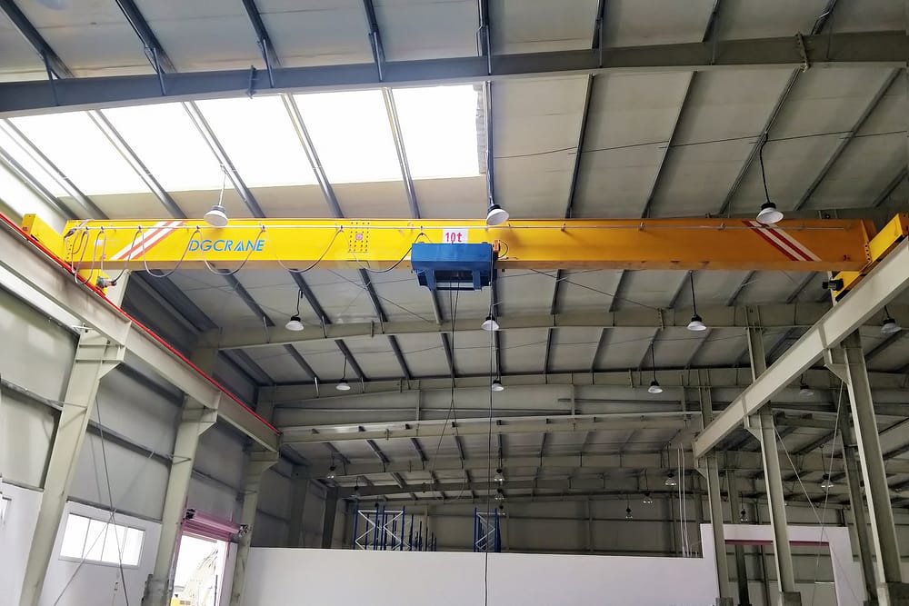 Een gele enkelligger-bovenloopkraan met het label DGCRANE met een capaciteit van 10 ton, geïnstalleerd in een industriële faciliteit met dakramen en stalen constructiebalken