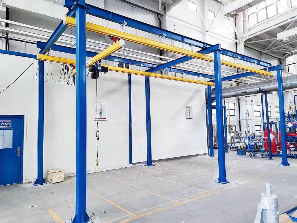 Een bovenloopkraansysteem voor werkstations met blauwstalen steunkolommen en een gele balk, voorzien van een takel, in een schone en georganiseerde industriële omgeving